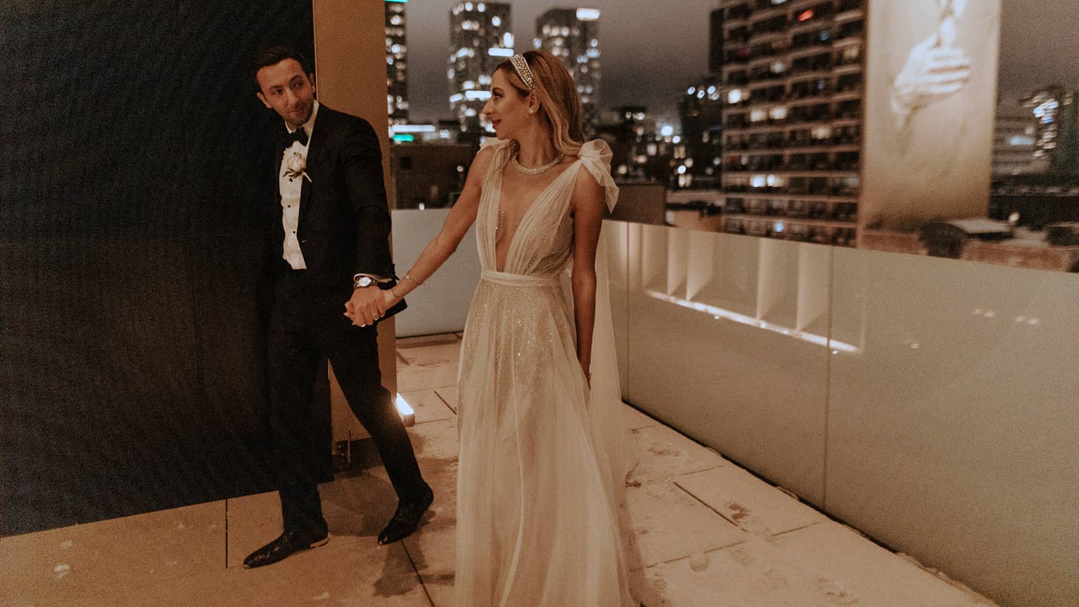 Bride and groom walk hand in hand on a rooftop terrace in Montreal, with the city skyline in the background