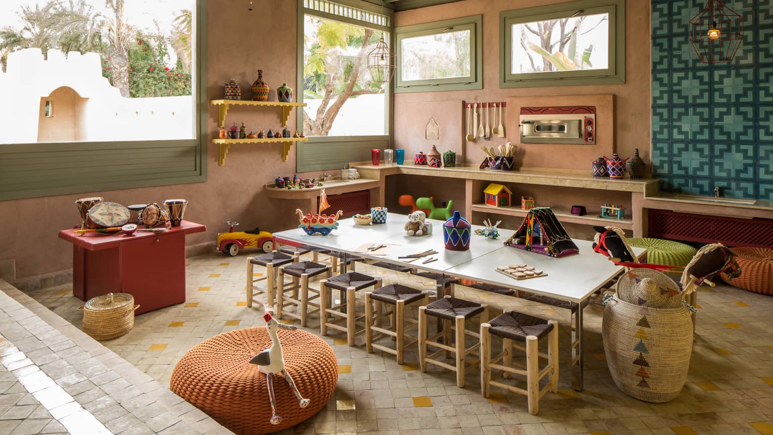 Kids Club long craft table with stools, toys on shelves along wall under sunny windows