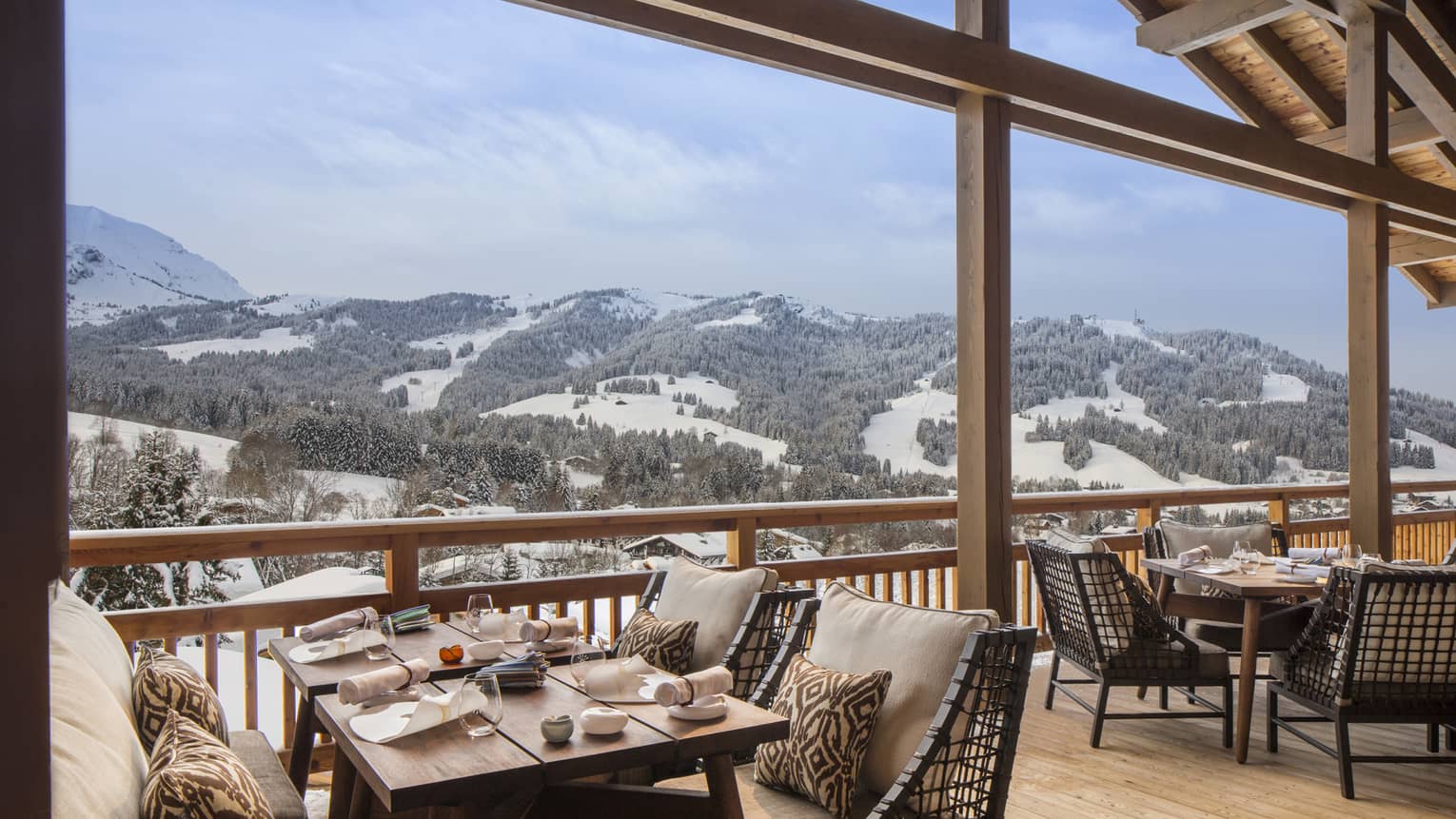 Dining tables, chairs, cushions under wood roof looking over snow-covered mountains