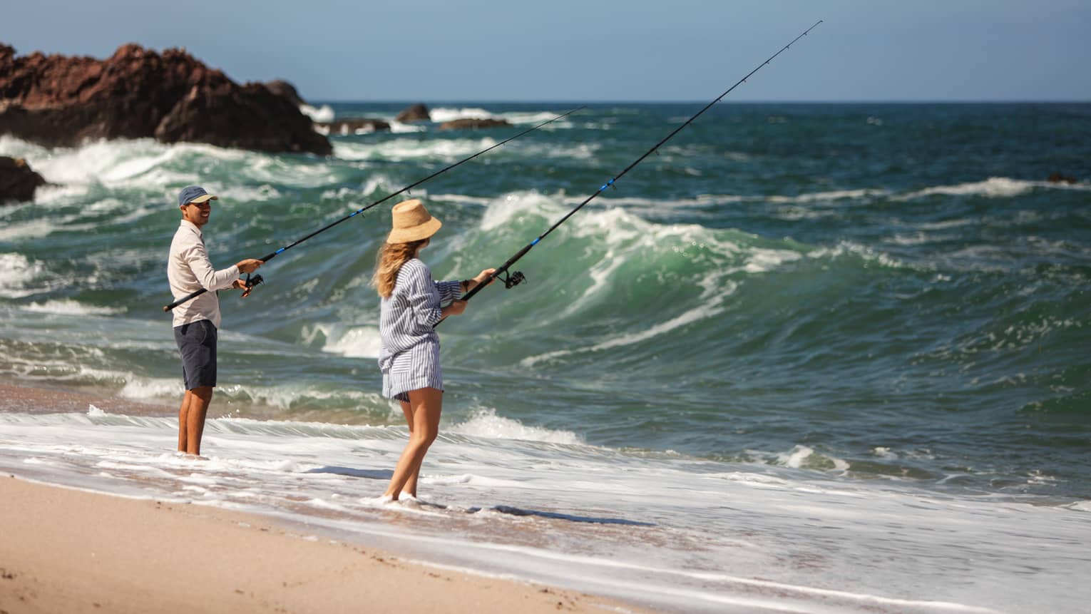 Two people fishing on a beach shore.