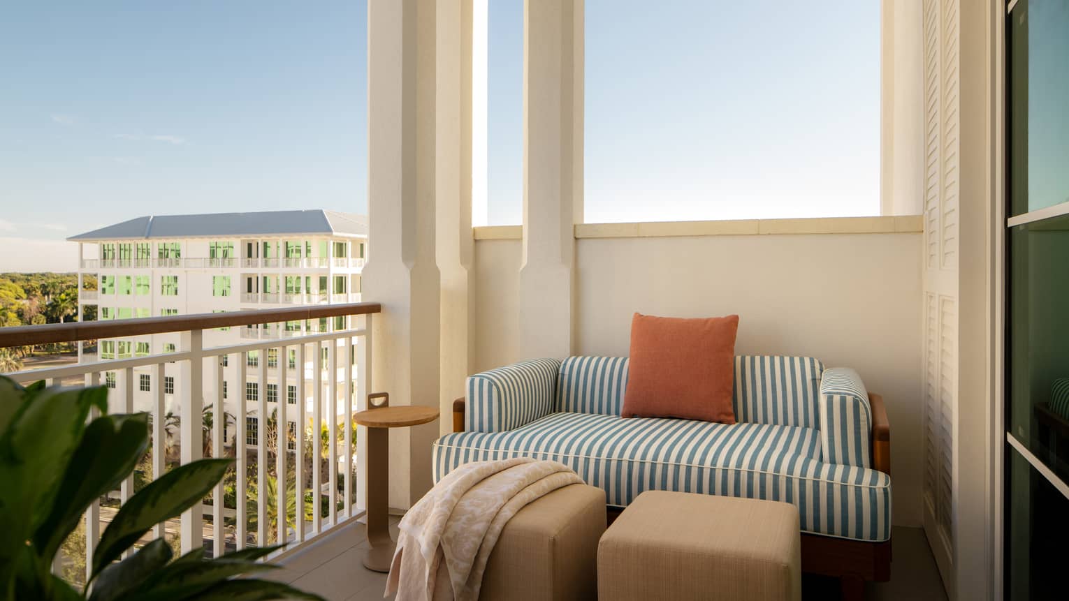 Hotel balcony with striped love seat and view of tropical resort