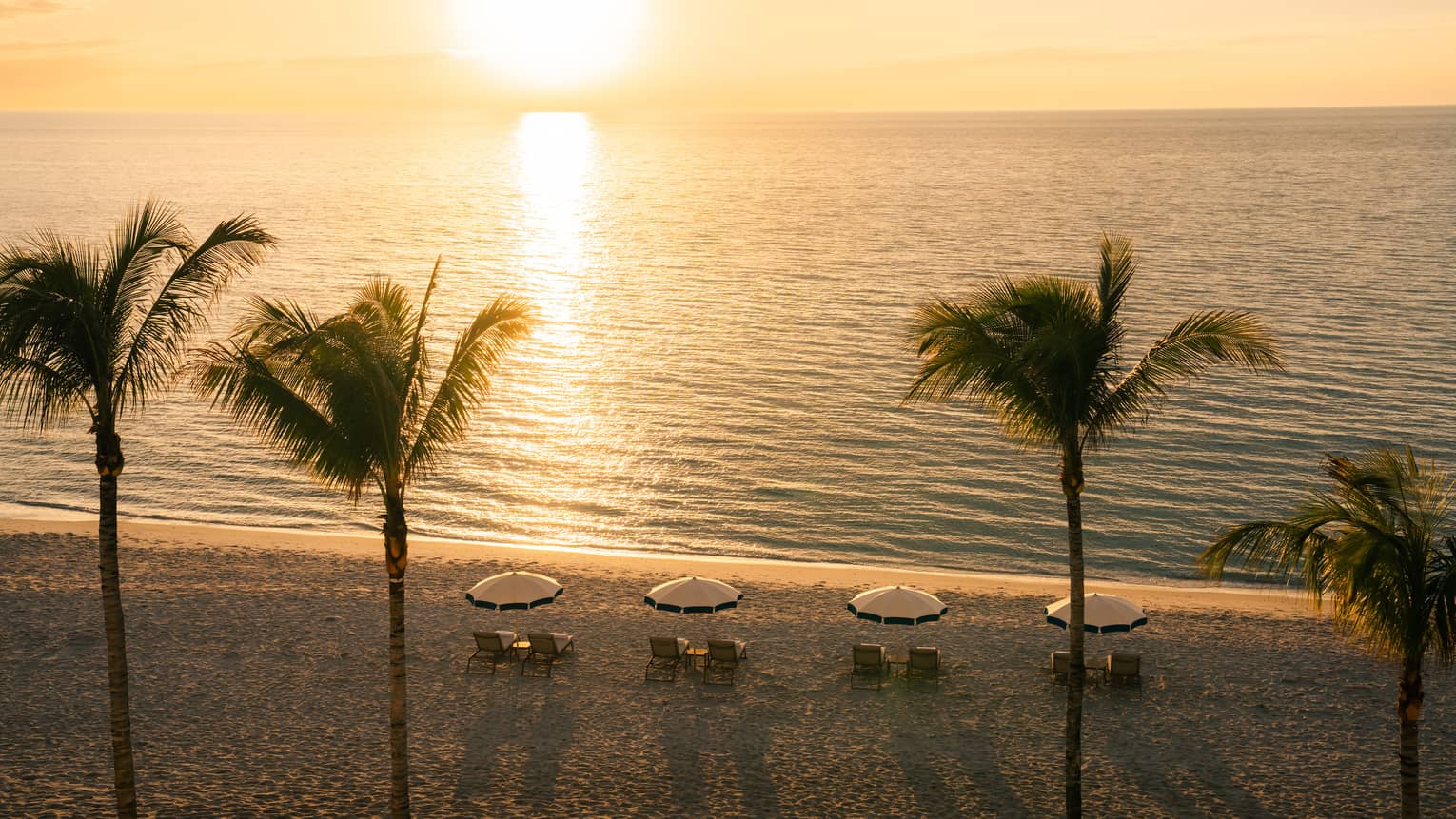 Aerial view of a private beach at sunset with four pairs of lounge chairs set up looking at the ocean