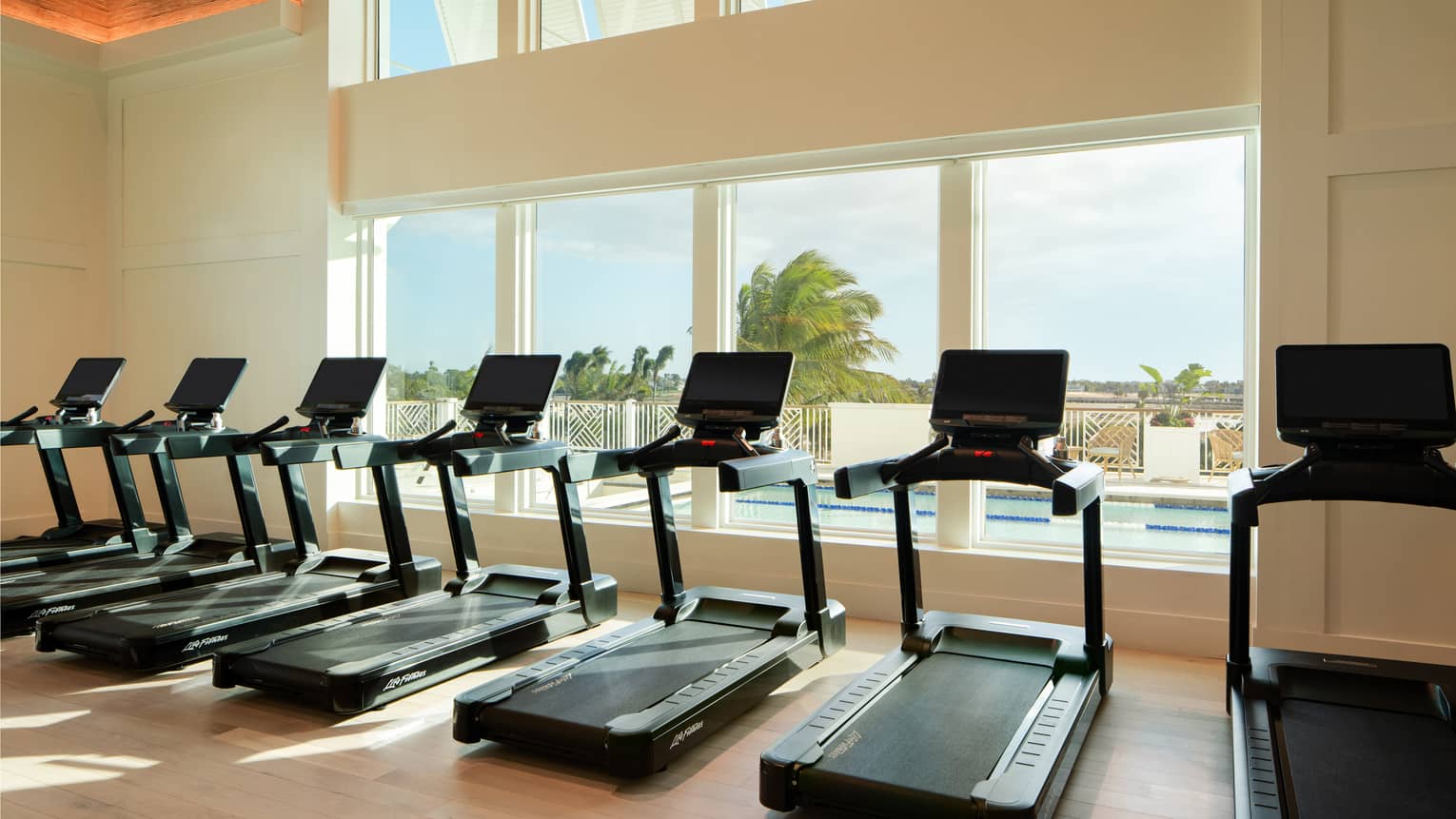 Row of treadmills lined up along a wall of windows overlooking an outdoor pool