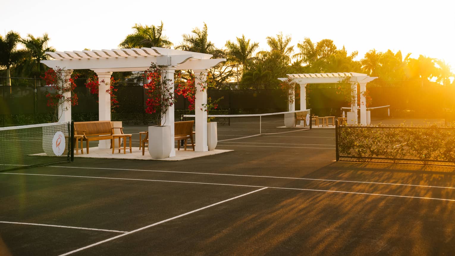 Three tennis courts with a white pergola and seating set between each court