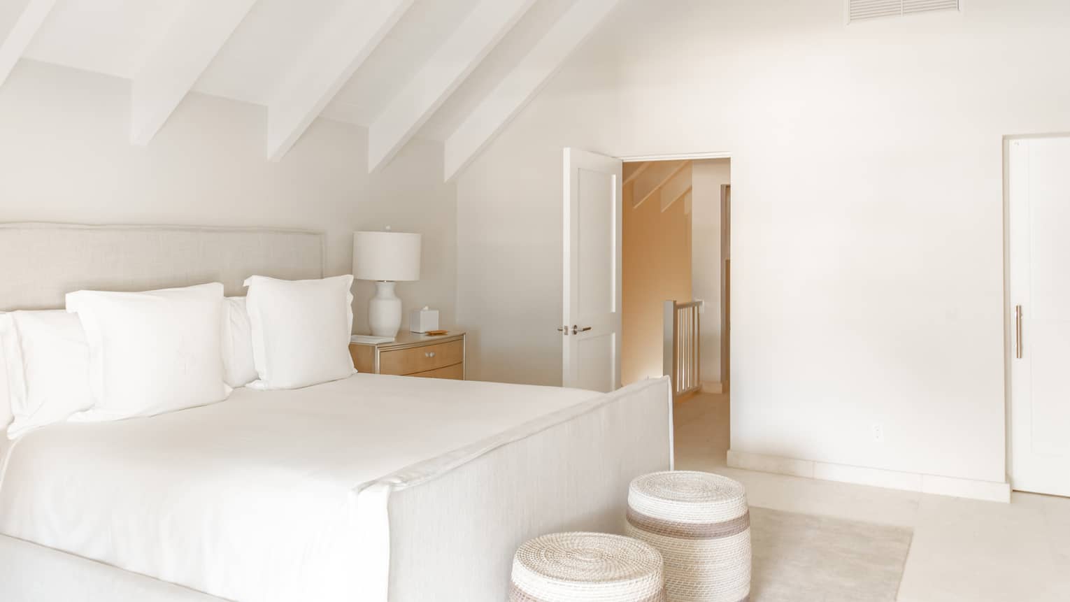 Bedroom with white walls, a white beamed, angled ceiling, and a king bed with white sheets