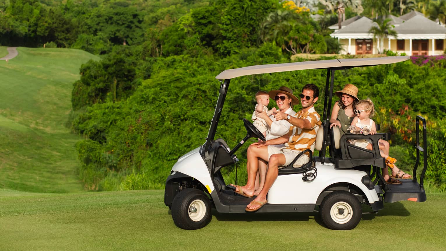 Five guests riding on a golf cart along a golf course