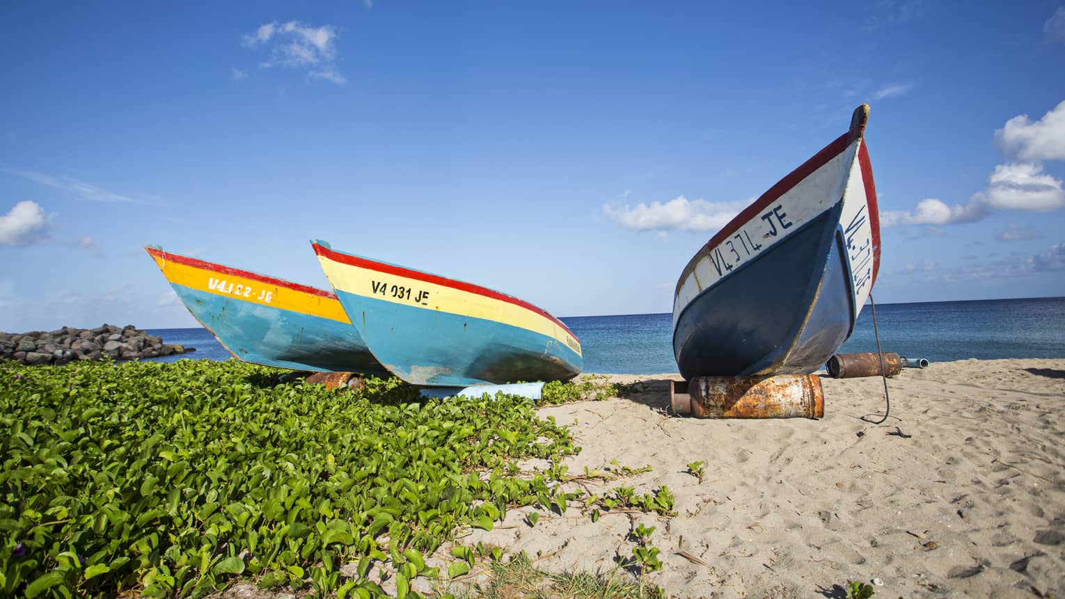 Three colourful boats parked on white sand beach against blue sky