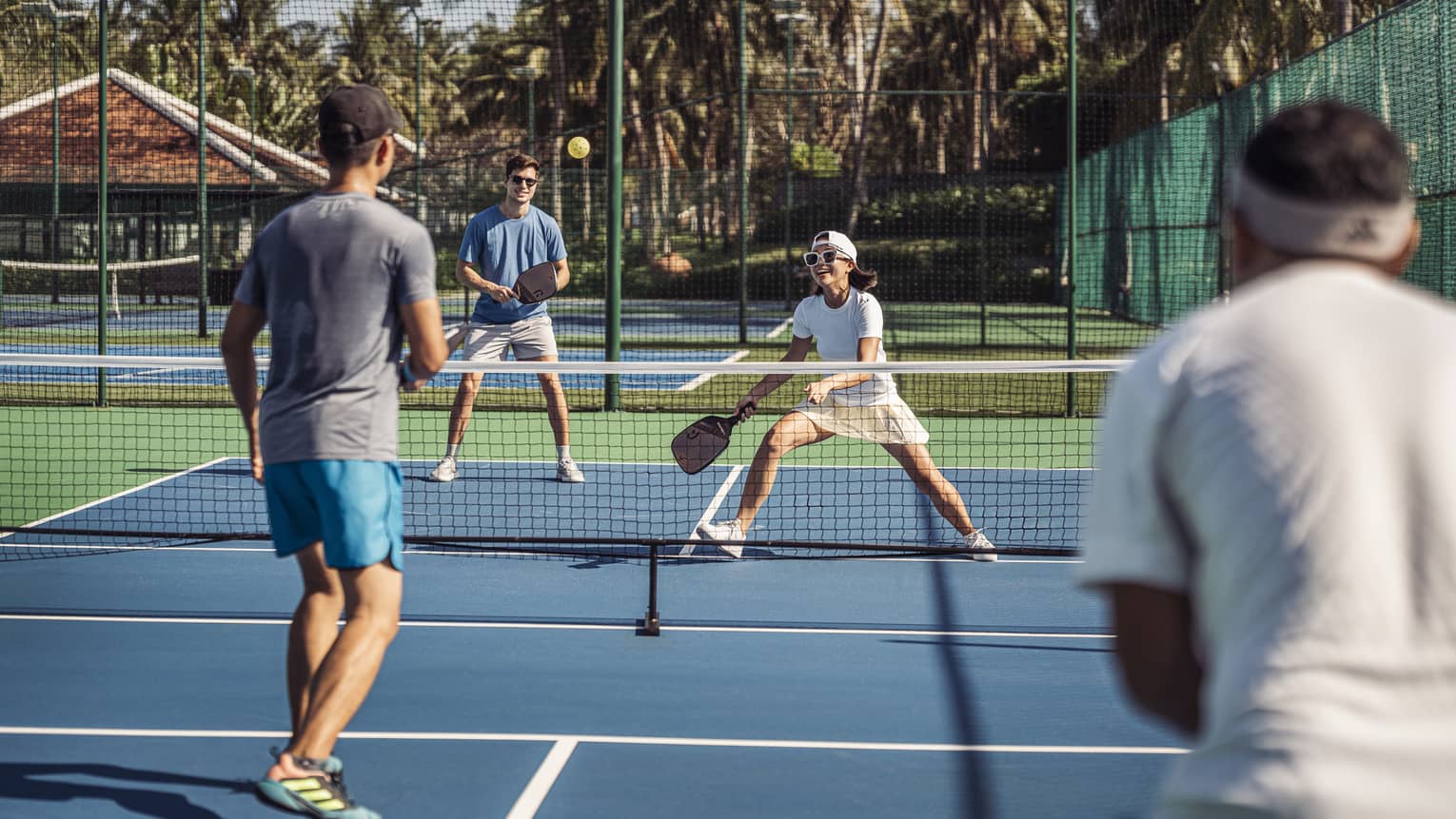 Group of 4 people play pickleball on artificial turf court