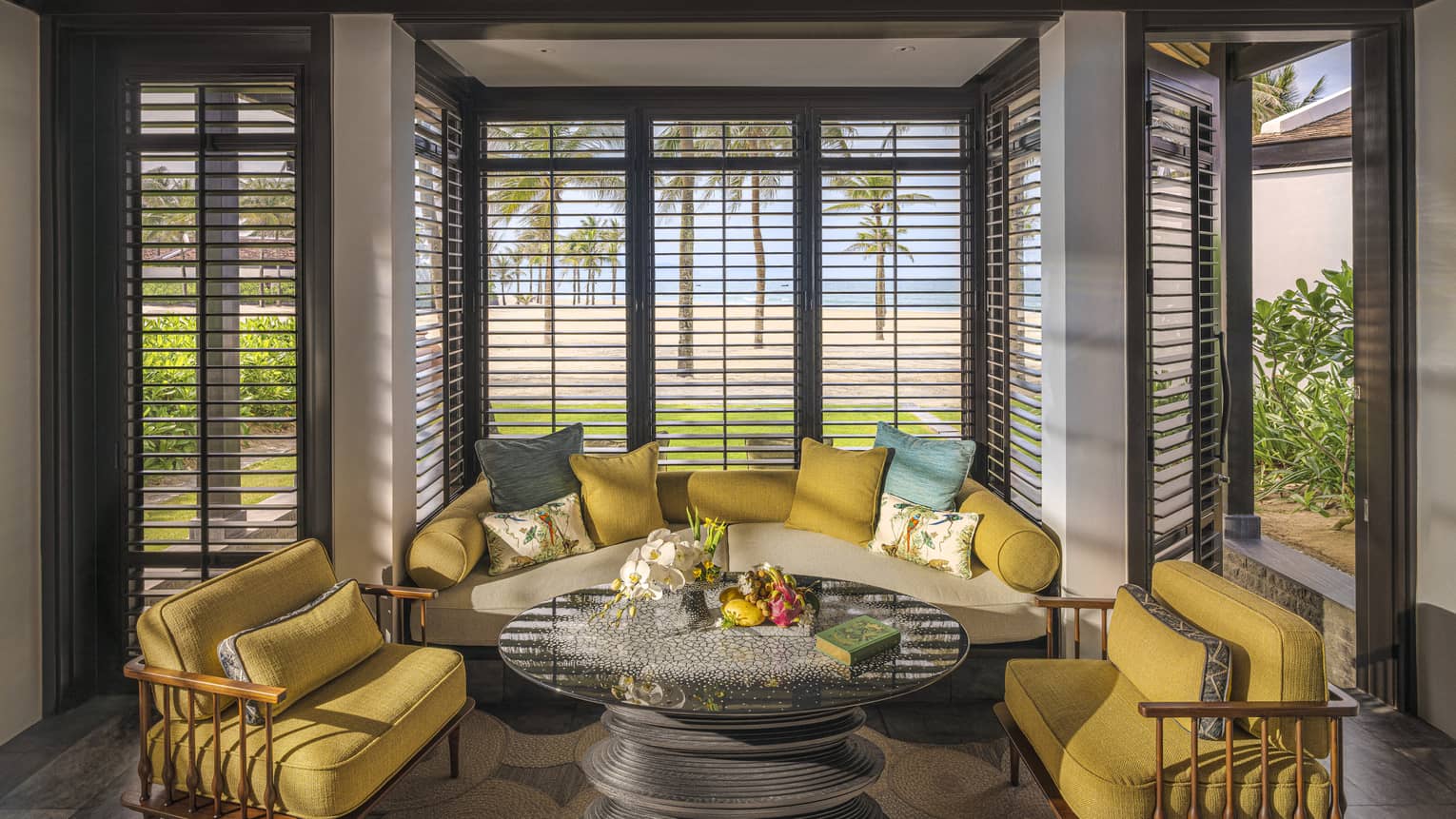 Guest room living area with mustard-coloured armchairs and sofa with floor-to-ceiling windows with. beach views