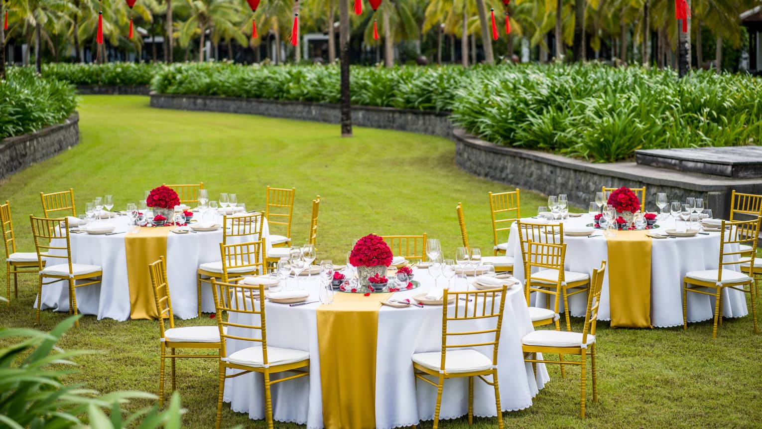 Three tables set out in the lawn with red lanterns for a wedding