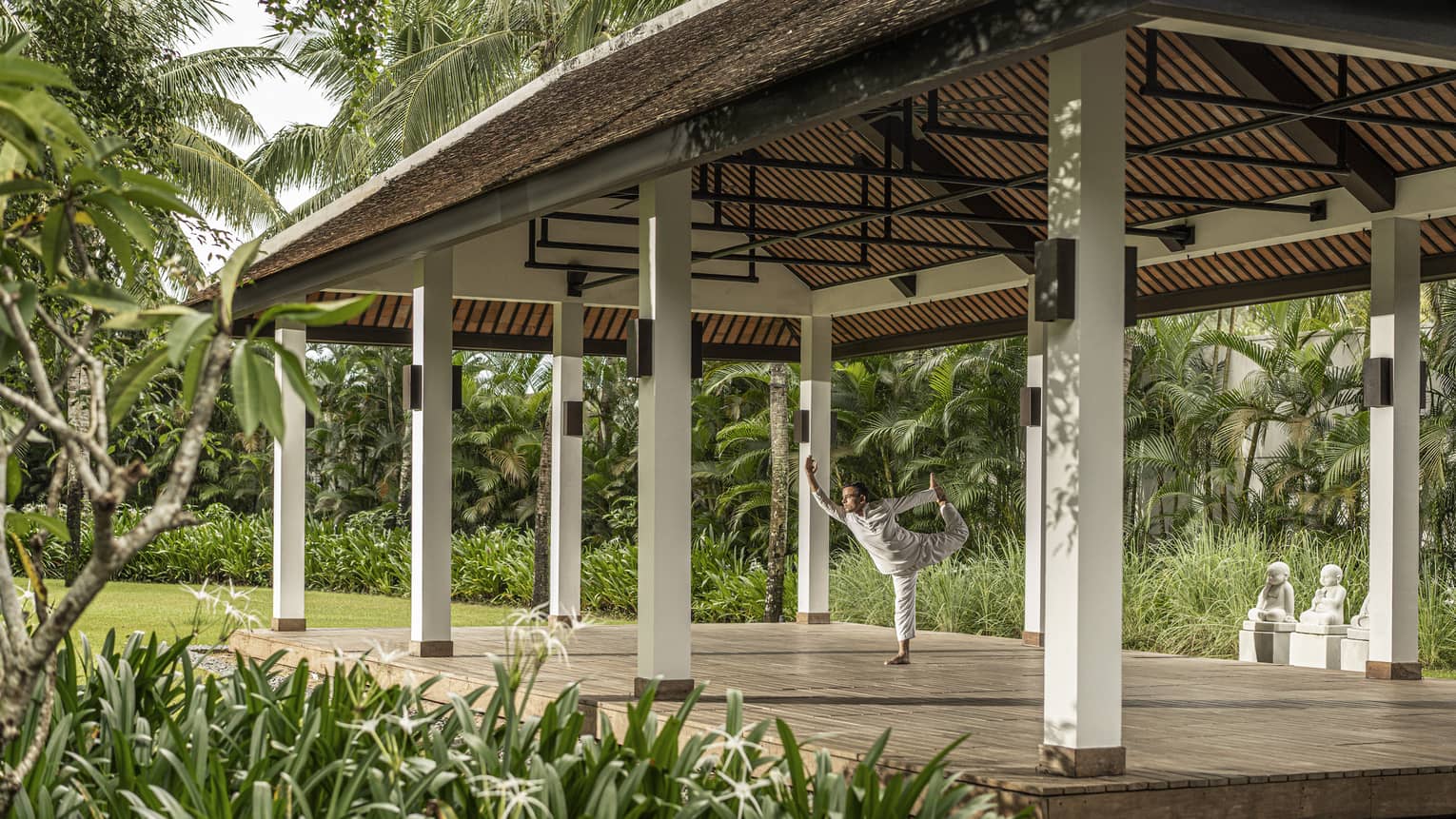 Man does yoga in outdoor yoga pavilion surrounded by palm trees