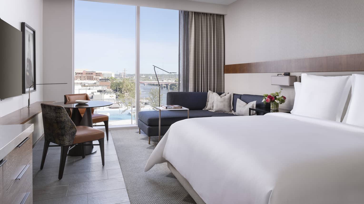 Guest room with a bed with white sheets, navy couch and floor to ceiling windows.