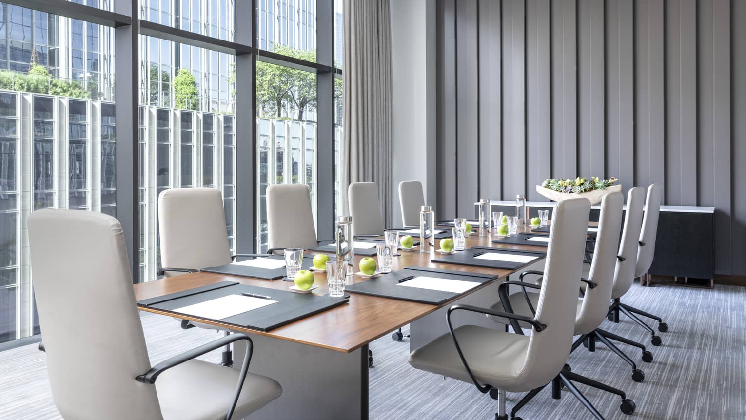 A meeting room with a large wood table, rolling chairs and a large window.