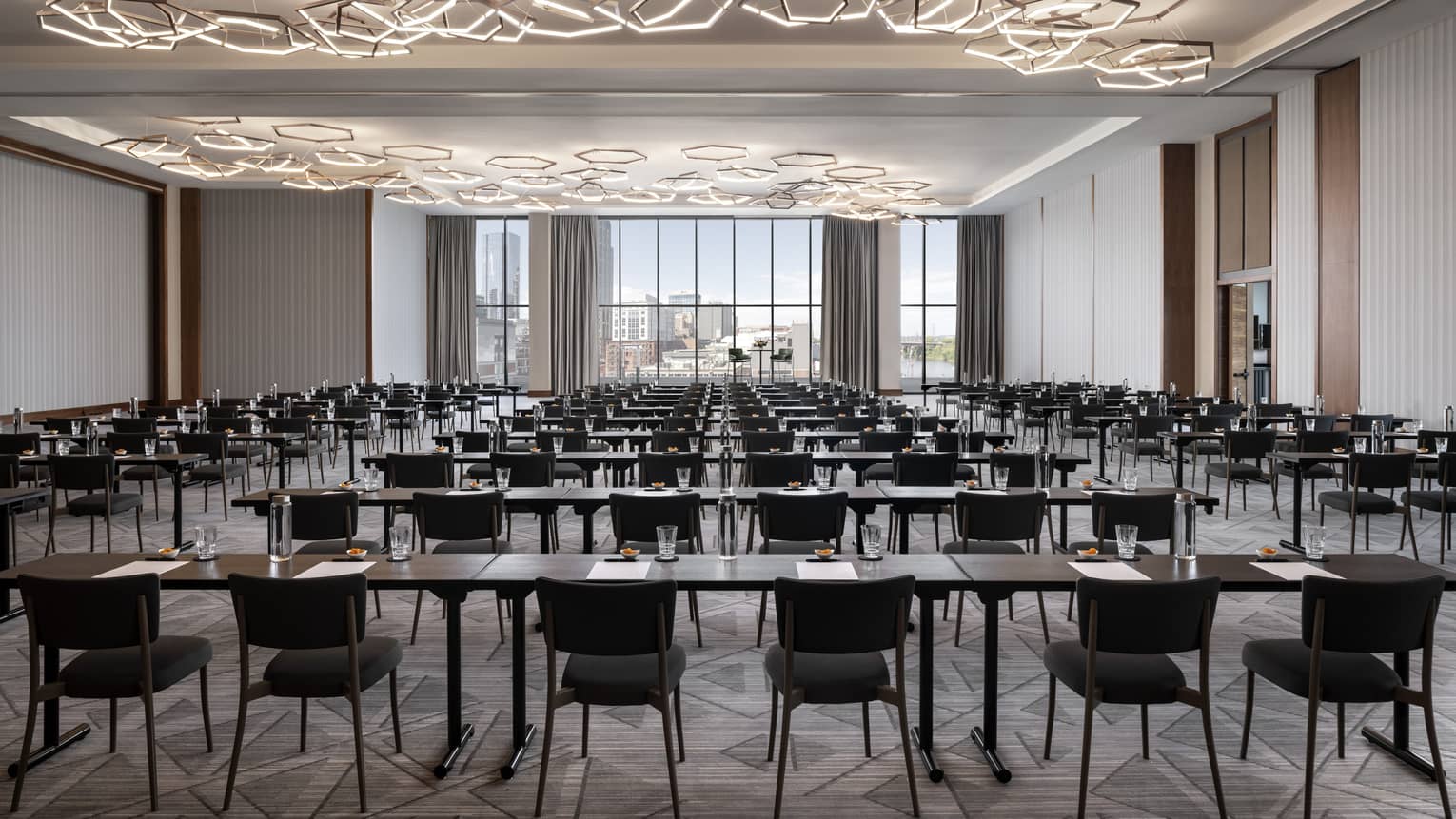 A large meeting room with many tables and chairs, geometric lights and large windows.