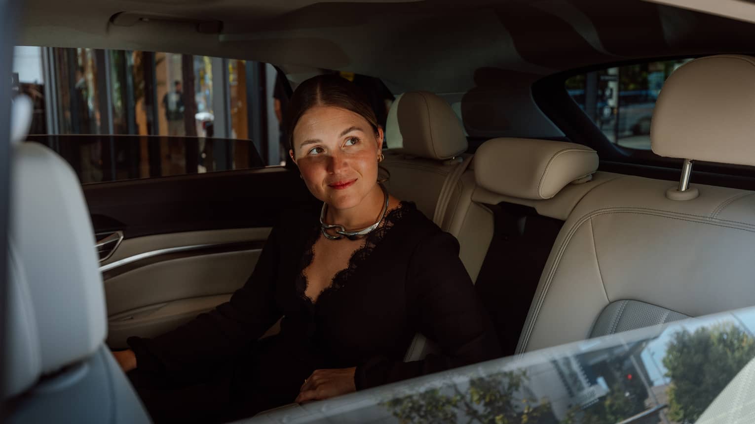 Person sitting in luxury vehicle backseat with windows slightly down
