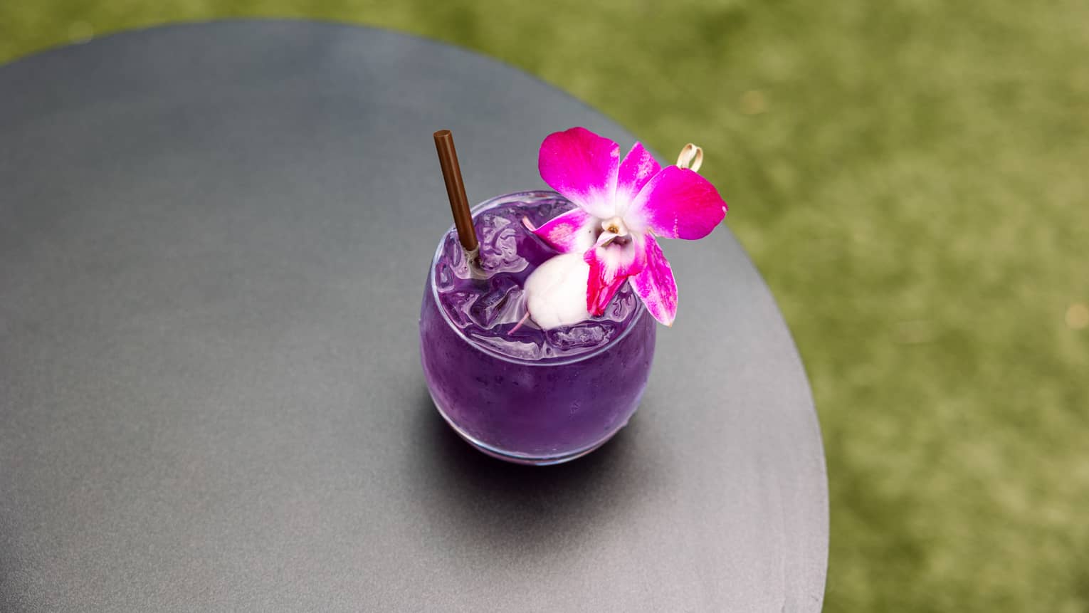 Purple alcoholic drink with a pink flower floating in it.