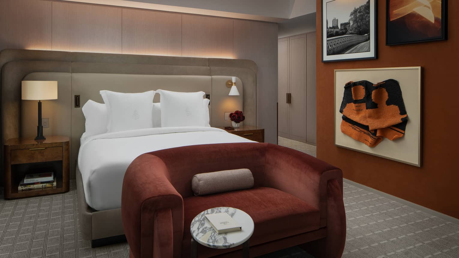 Hotel bedroom with king bed, deep red velvet love seat and three pieces of artwork on the wall