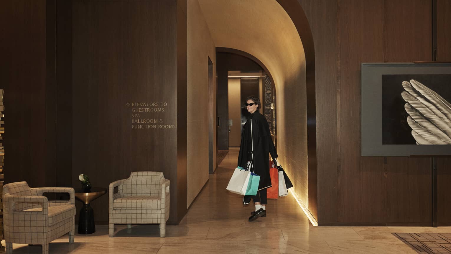 Woman dressed in black clothing and sunglasses, carrying shopping bags.
