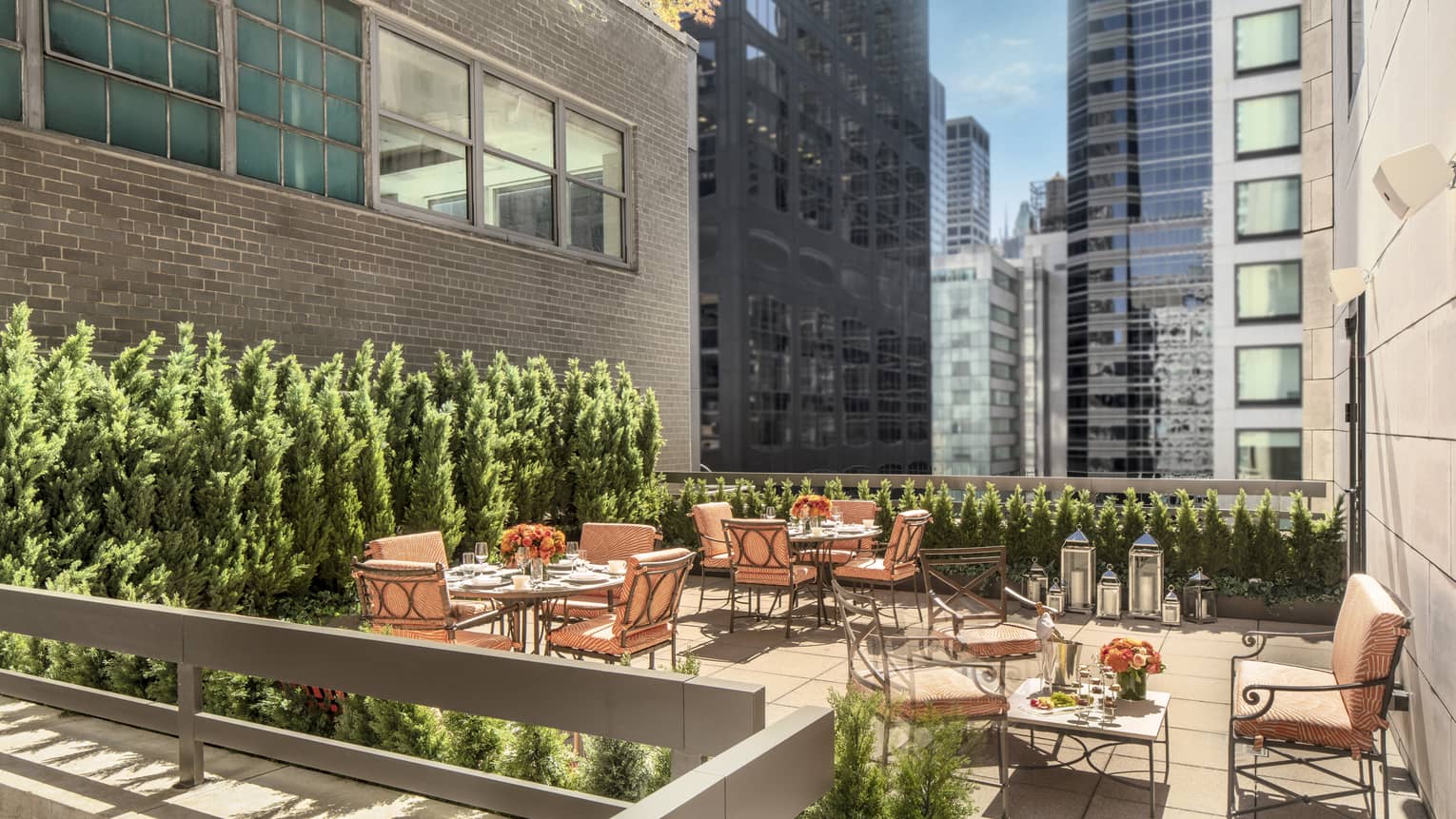 11th Floor Terrace Boardroom, surrounded by green topiaries, with square iron and glass tables with orange cushions on chairs at Four Seasons Hotel New York