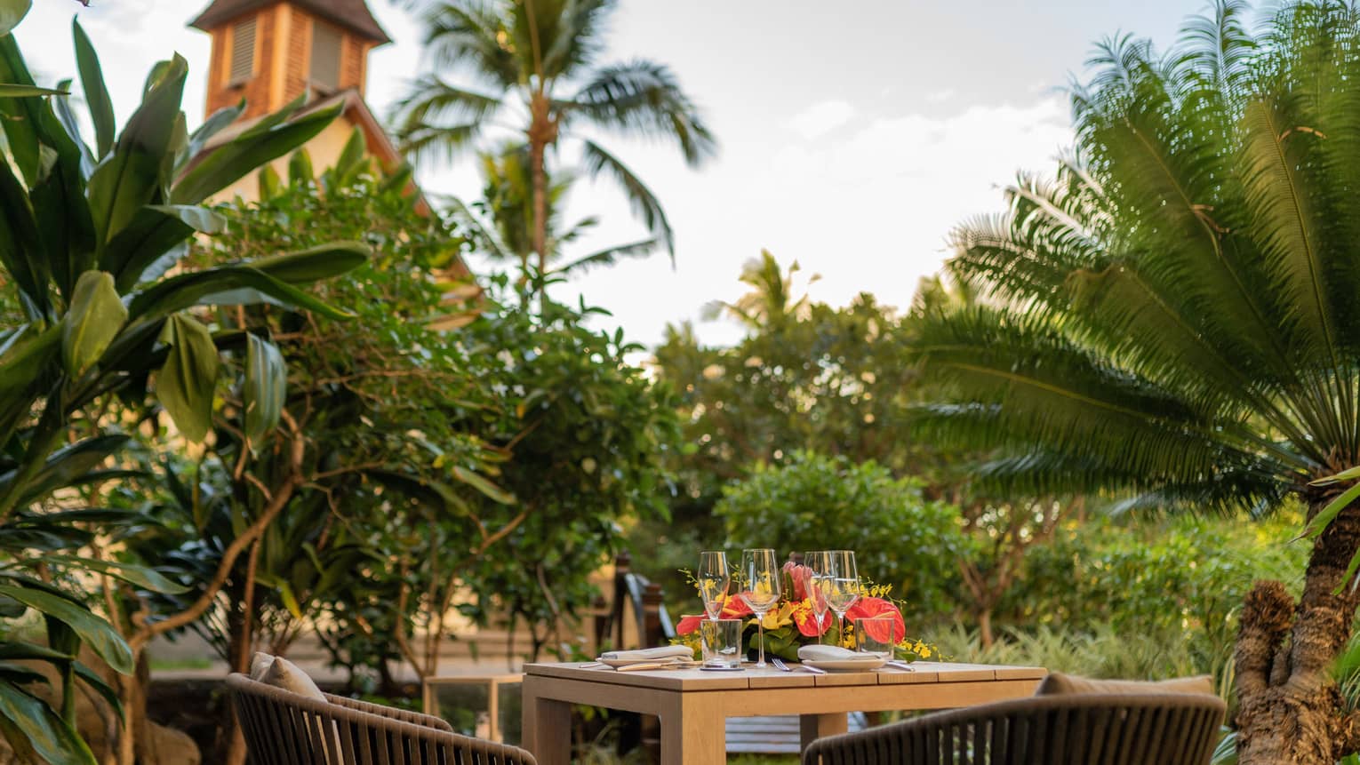 Wooden table set for a two-person dinner in private, tropical garden setting