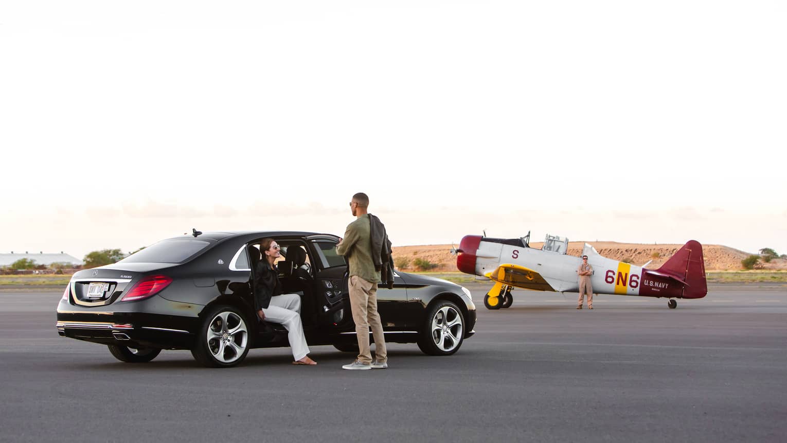 Two people getting out a car near an old plane.