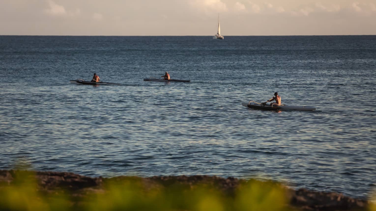 Three kayakers in the ocean with a sailboat in the background