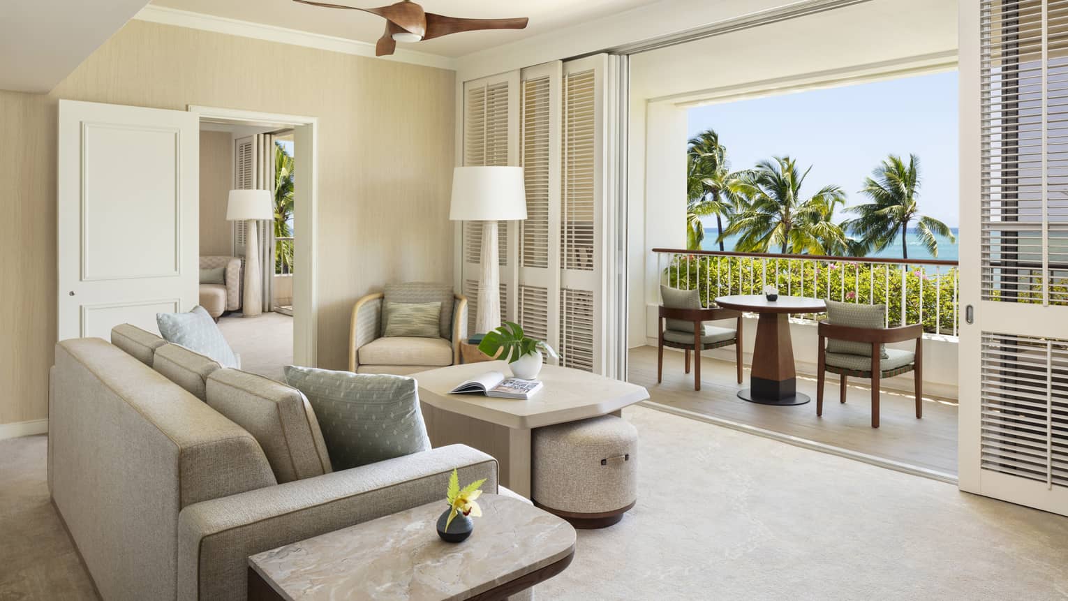 Elegant resort suite living room, featuring a beige sofa facing a furnished balcony with tropical ocean views