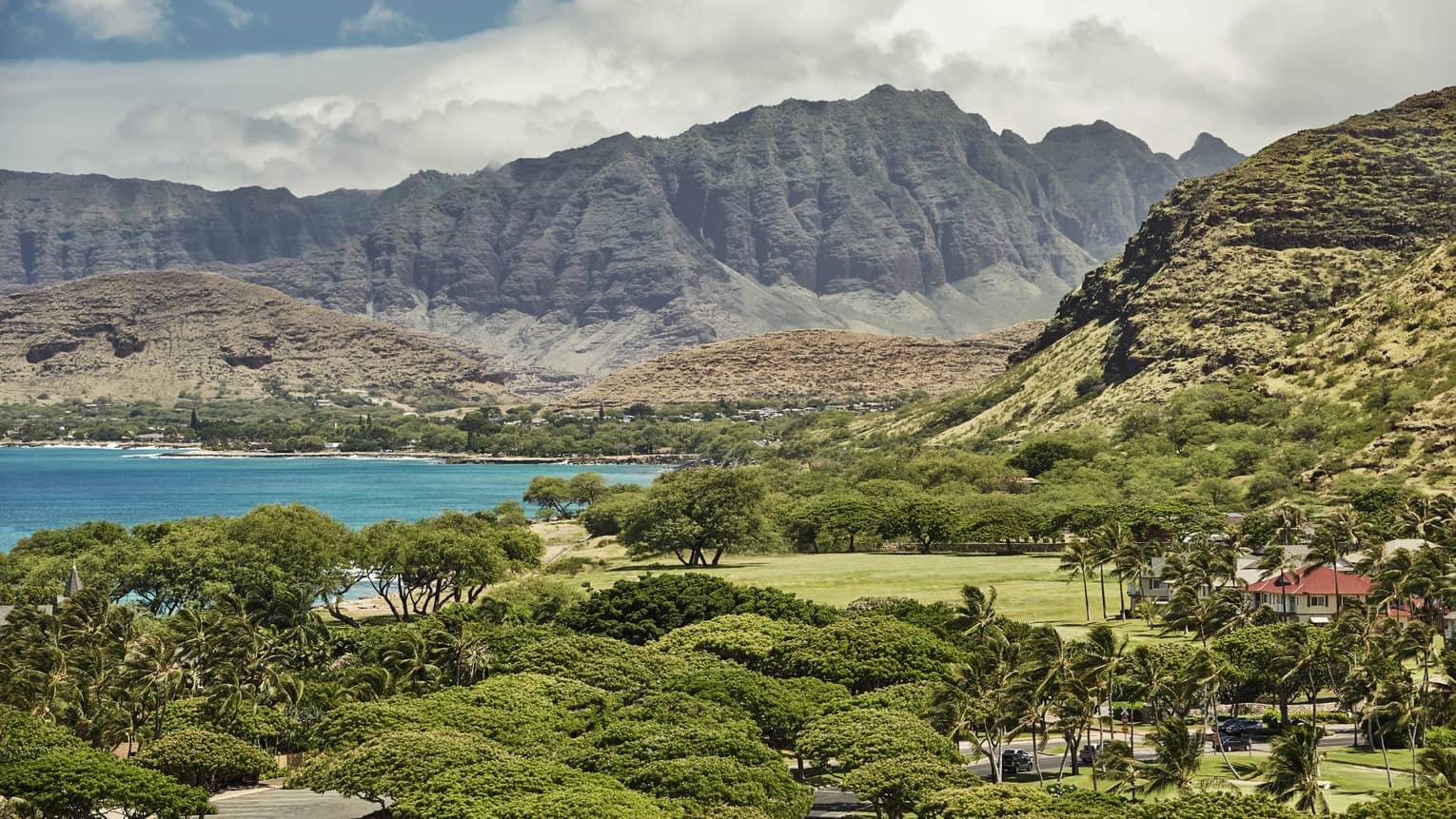View over trees, manicured resort lawns, bleu ocean below sweeping mountains