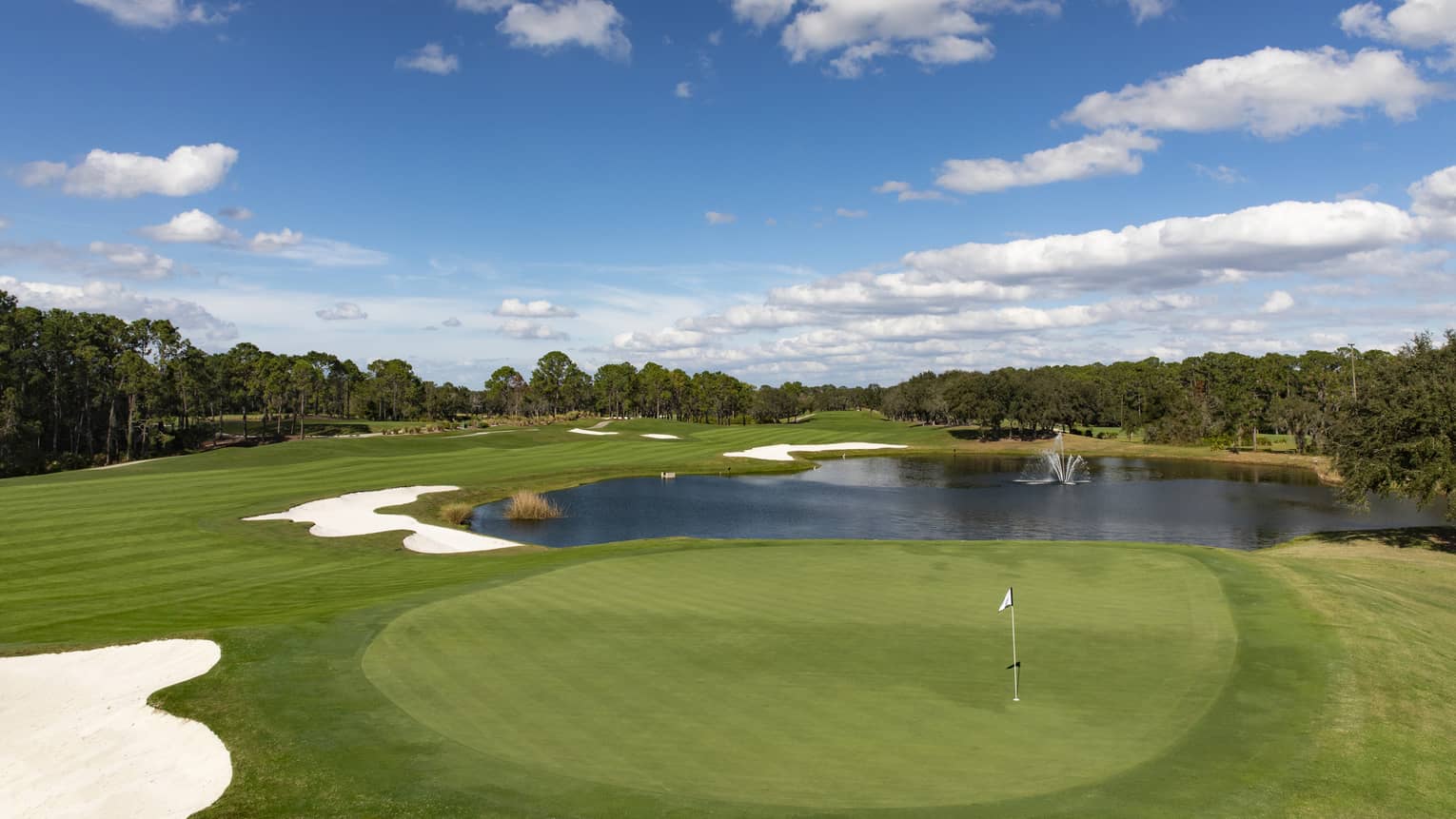 View across golf course green, small pond under blue sky 