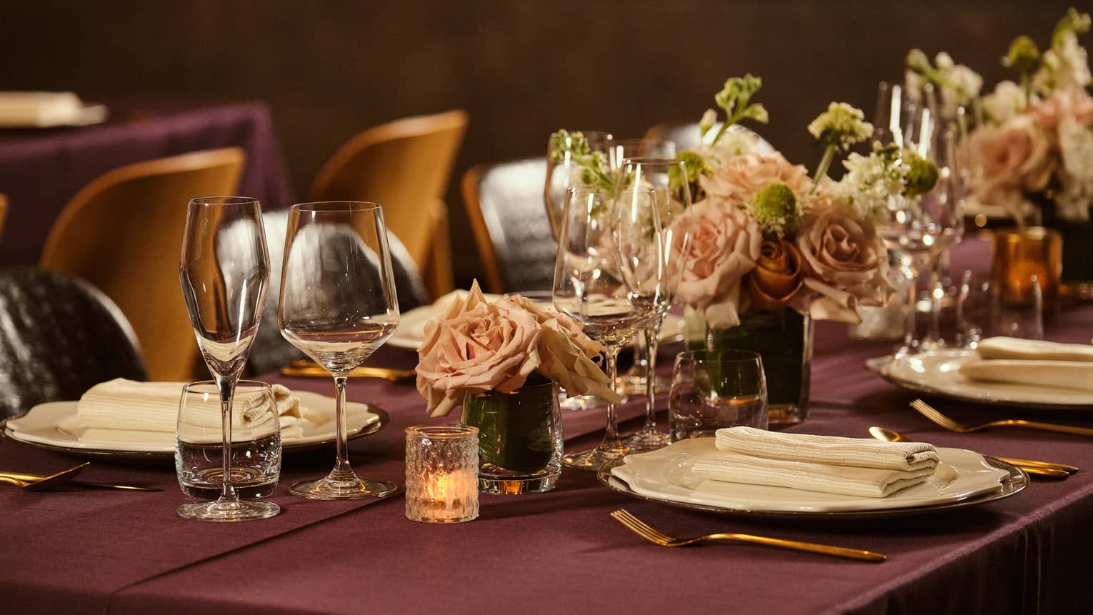 Table set with a burgundy tablecloth, votive candles and small vases filled with light-pink roses