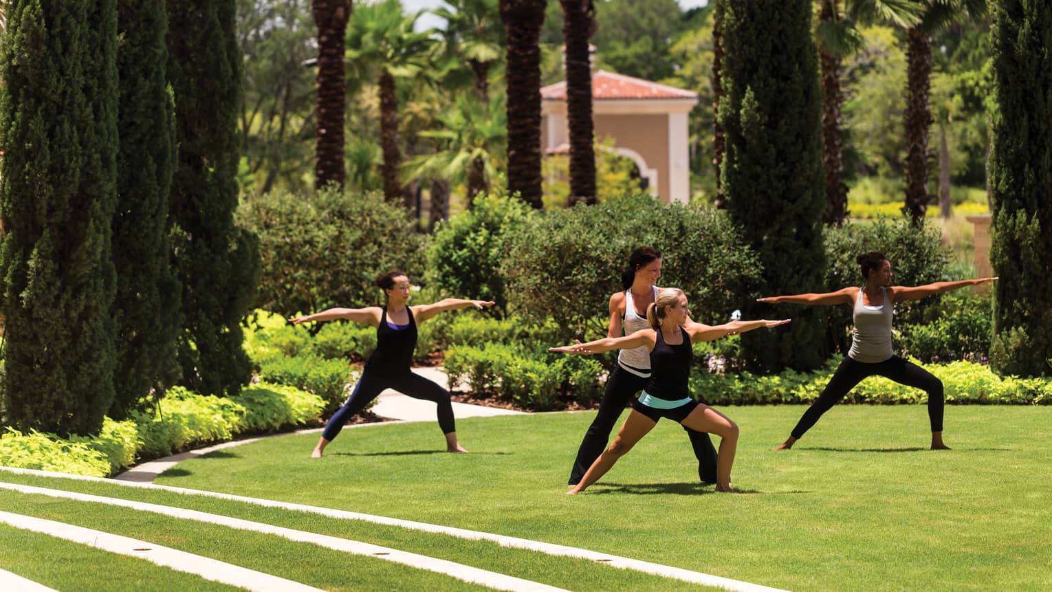 Group of people stand, arms outstretched in yoga poses on green lawn