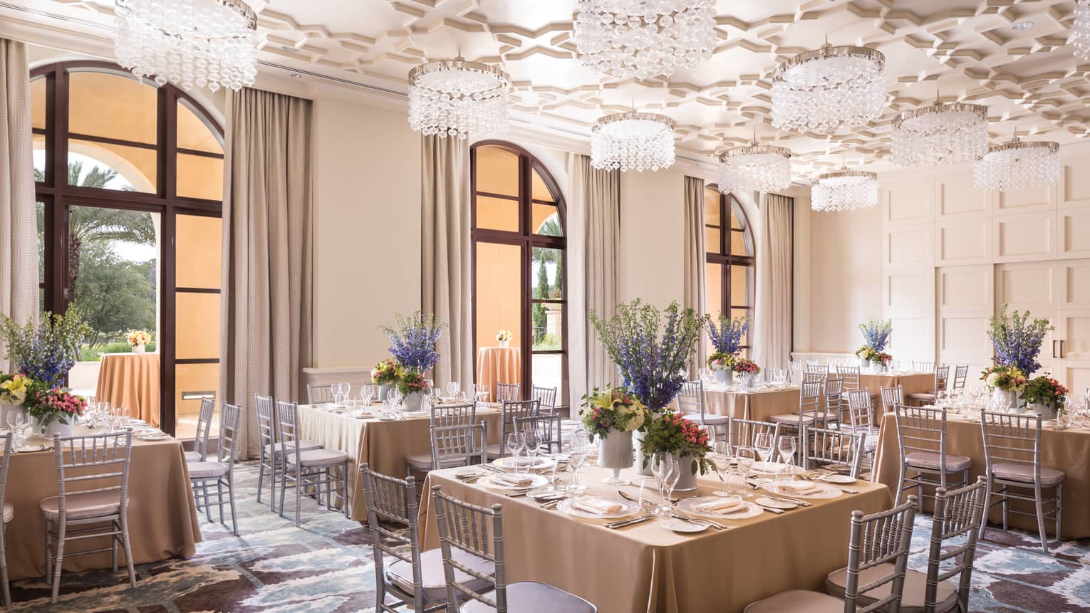 Square banquet dining tables under geometric ceiling with crystal chandeliers 