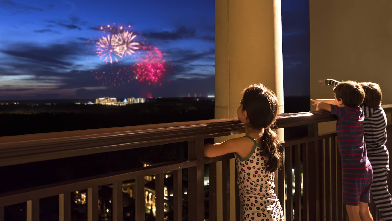 Young girl stands on Four Seasons Hotel balcony, watches colourful fireworks display over Walt Disney World resort