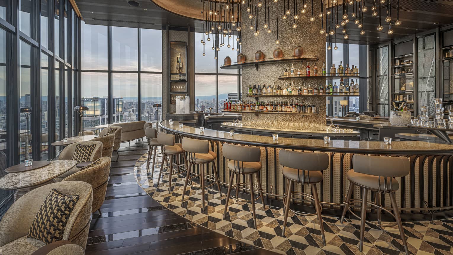 Large circular granite-topped bar in a modern luxury restaurant surrounded by a bank of windows overlooking city at dusk.