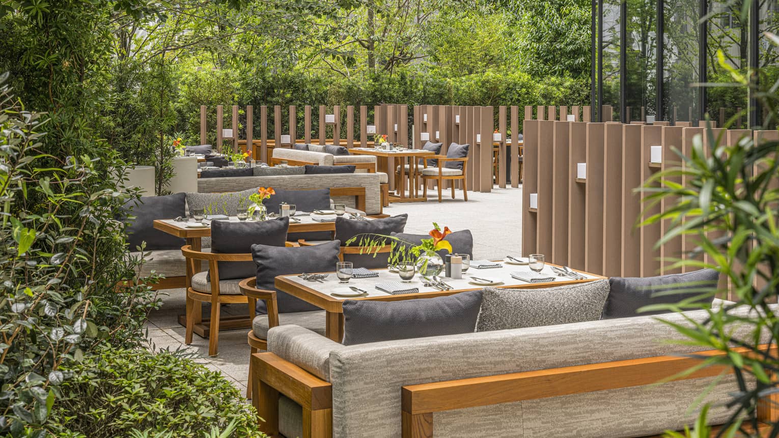 Large restaurant terrace with casual yet luxurious cushioned divan and chair seating set amid lush green trees and shrubs.