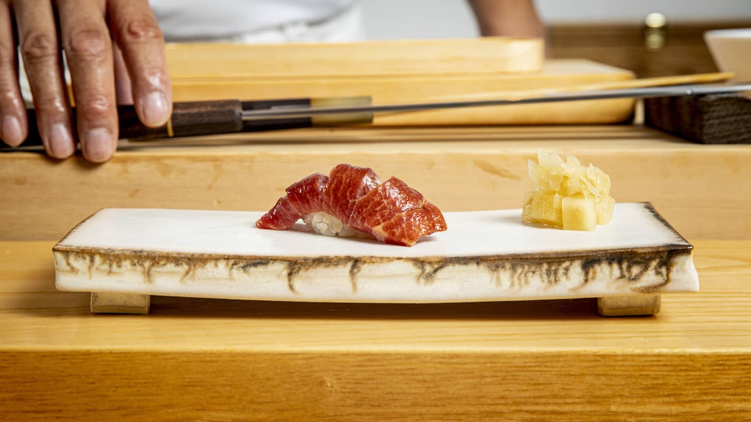 Edomae sushi on a modern stone plate, with a chef and chef's knife in the background