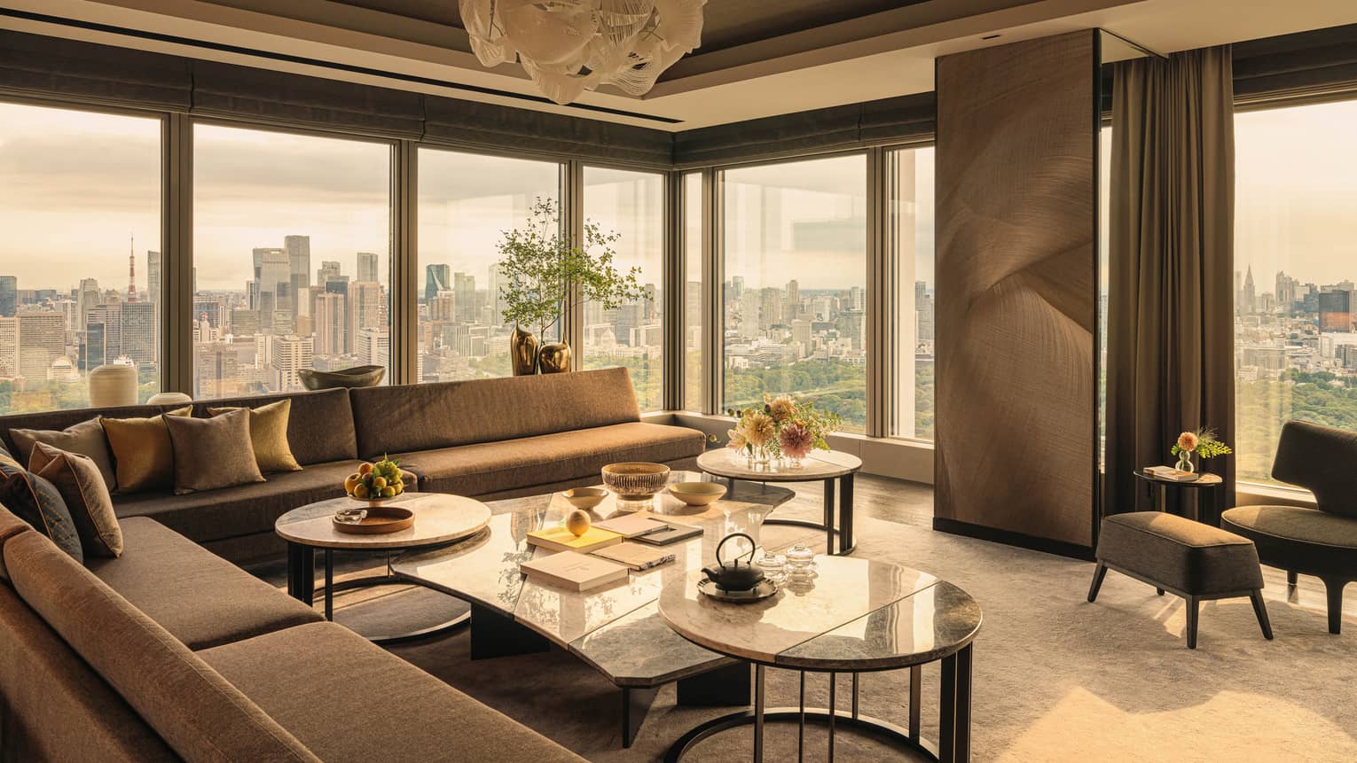 Luxury hotel suite featuring sectional sofa, a cluster of coffee tables, modern lighting fixture and city views