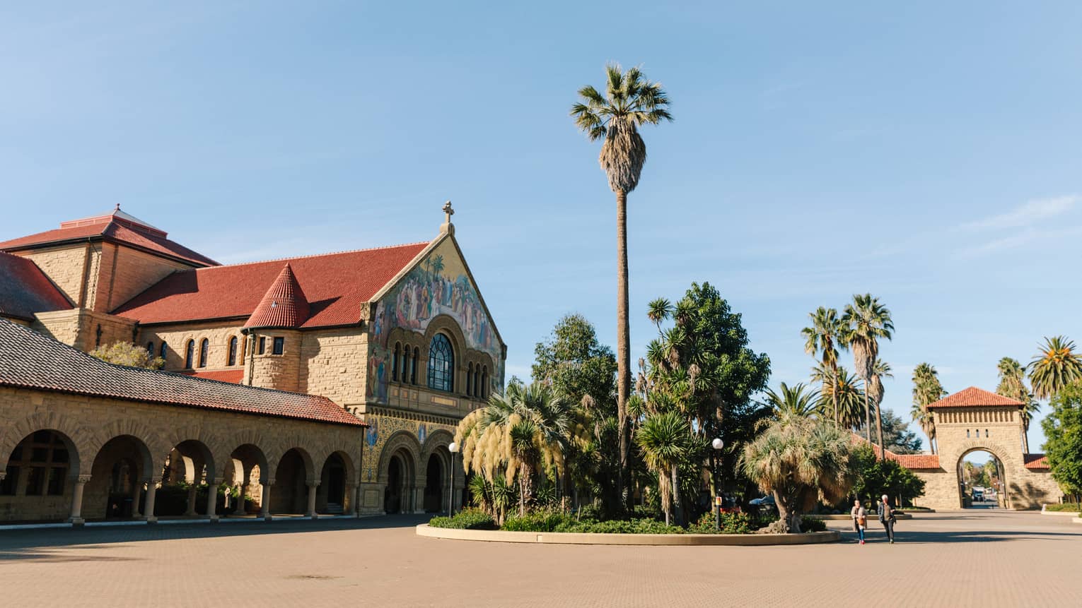 Palm trees next to a large brown and red building on a sunny day.