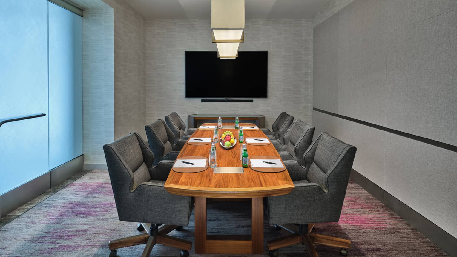Room with gray chairs and a rectangular table and a monitor on the wall.