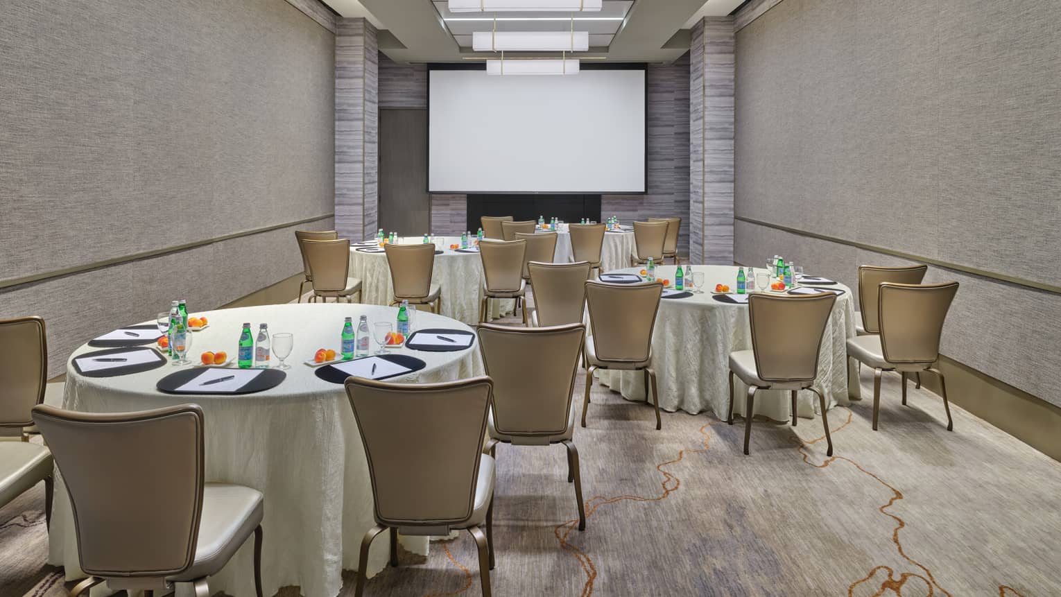 Event room with four tables with beige table cloths and a projector screen.