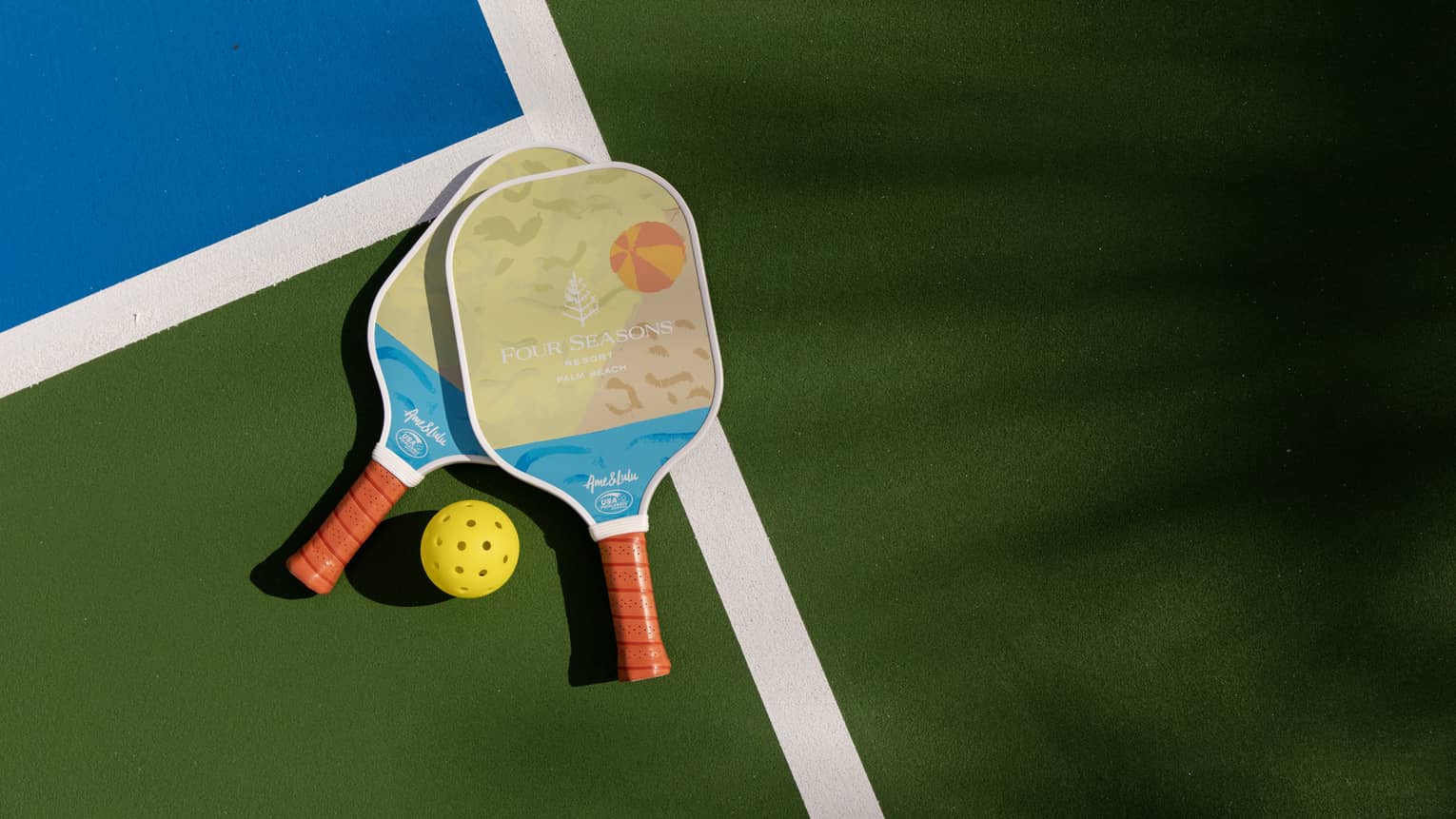 Two pickleball paddles and a yellow pickleball rest on a court