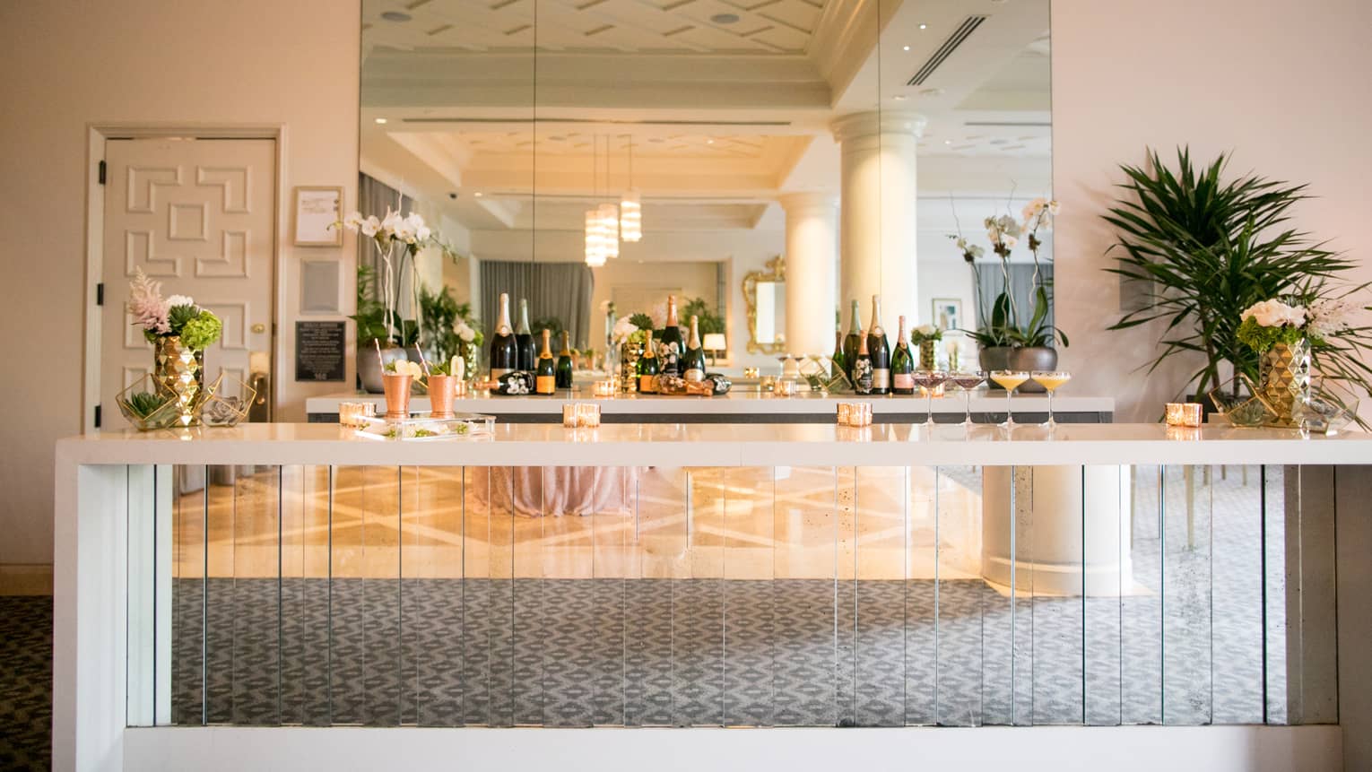 Champagne bottles on shelf under mirror behind elegant glass cocktail bar 
