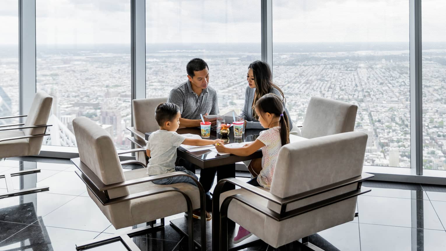 A mother and father with two kids at a table near large windows.