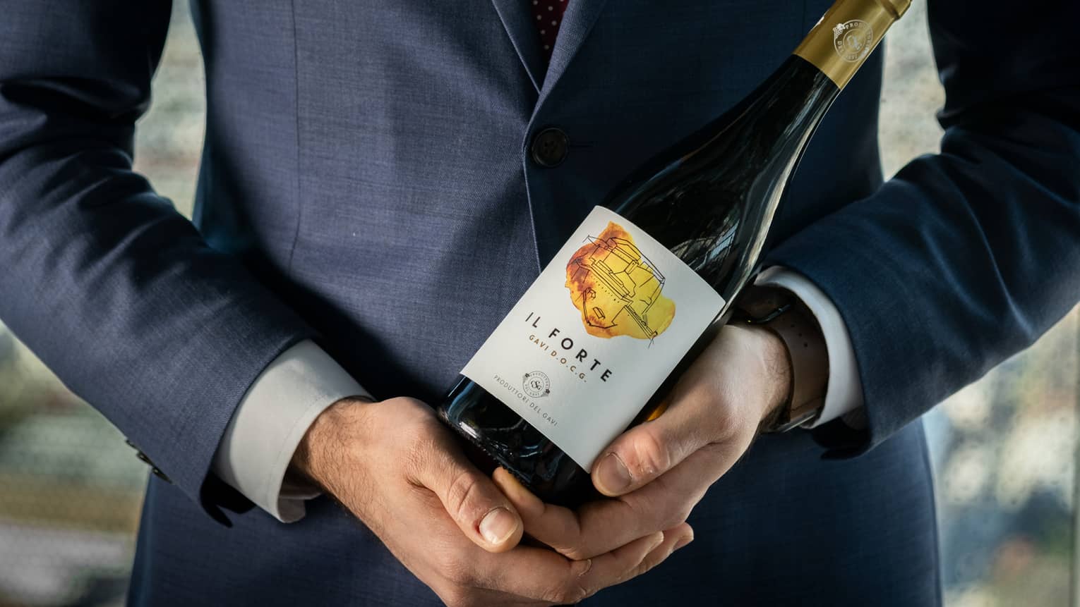 A man in a dark blue suit holding a bottle of wine.
