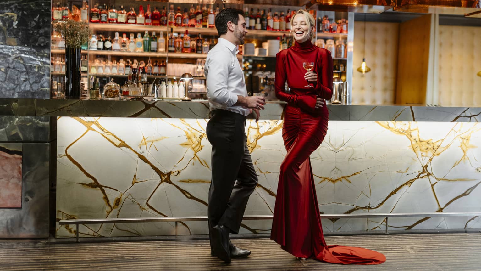 Couple standing, laughing in front of a dimly lit stocked bar