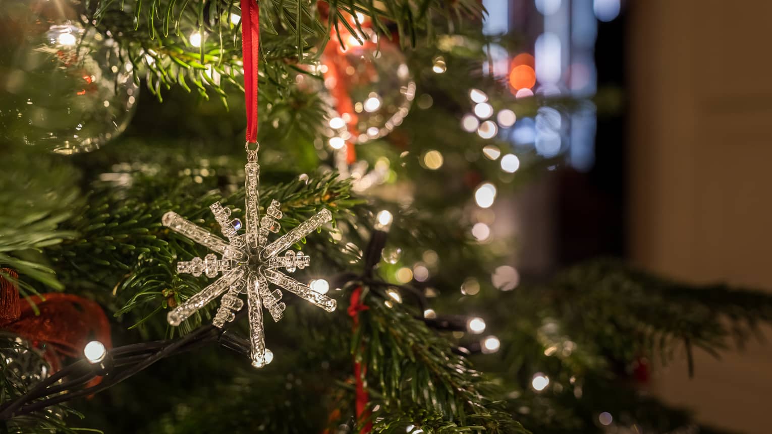 Close-up of a crystal snowflake ornament hanging on a Christmas tree with festive lights in the background