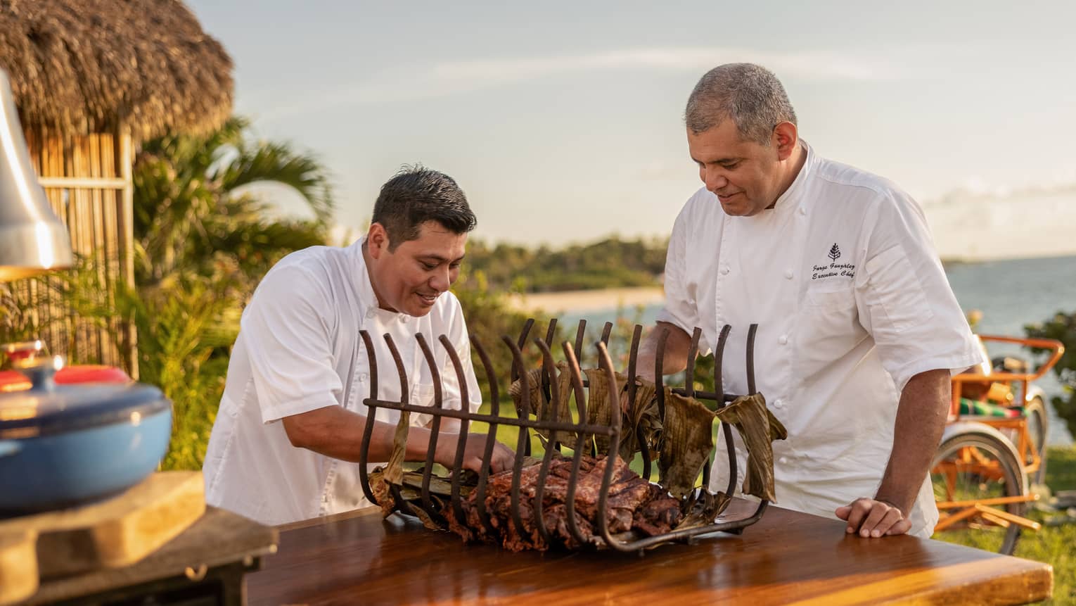 Two chefs prepare food in an outdoor cooking space.