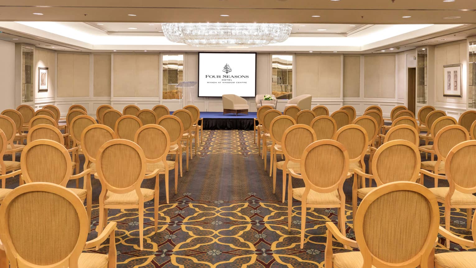 Conference meeting room with chairs facing slightly elevated stage and screen