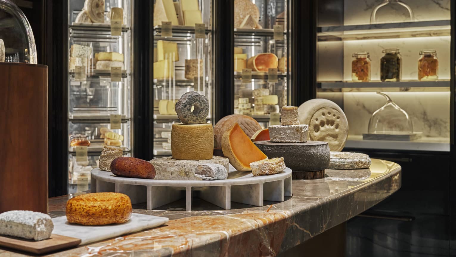 Various wheels and blocks of cheese displayed in tiers on a marble counter