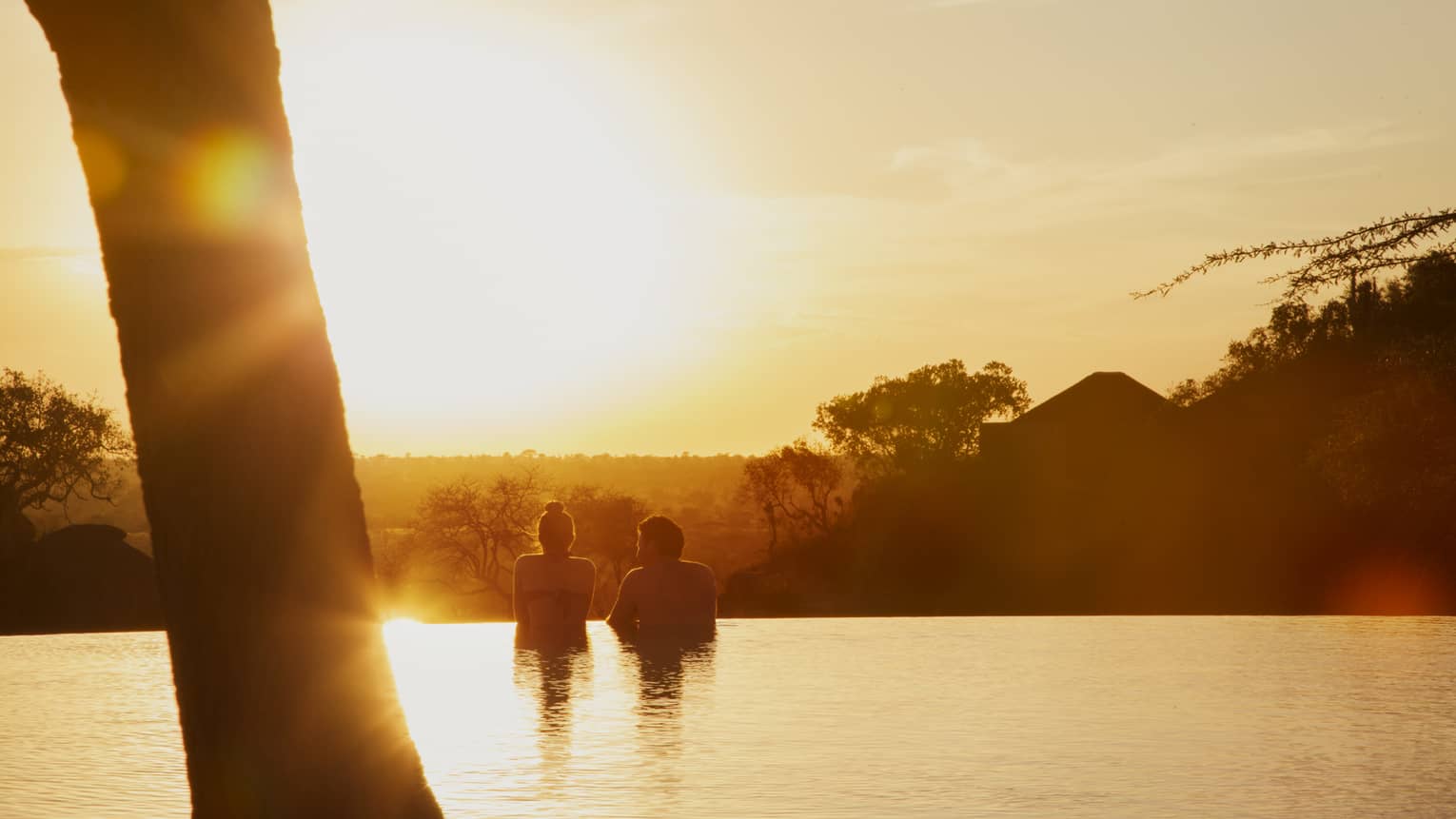 Silhouettes of couple wading in infinity swimming pool at sunset